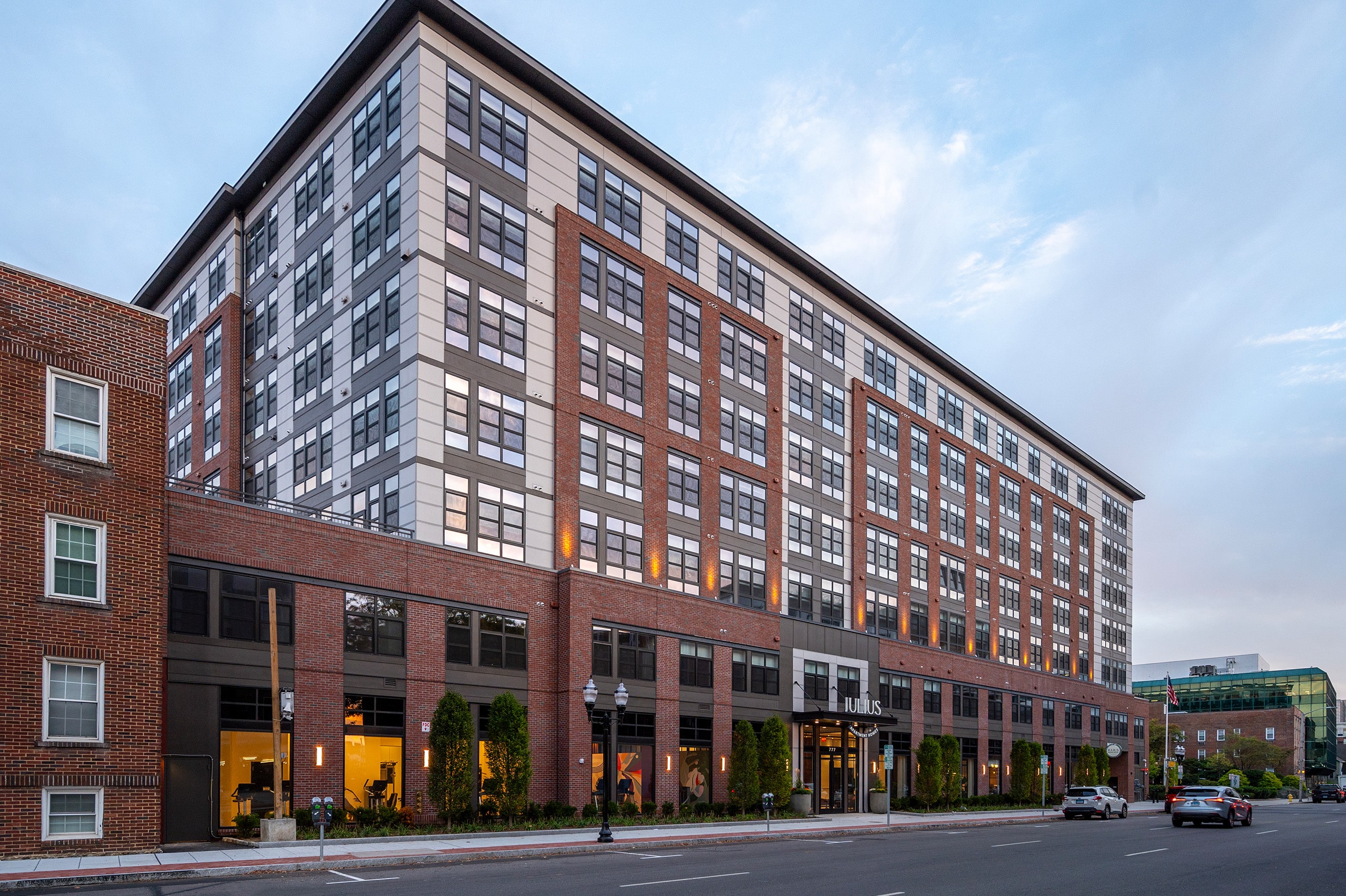 Exterior of an apartment building with a facade of red brick, light grey stone, and black-framed windows.