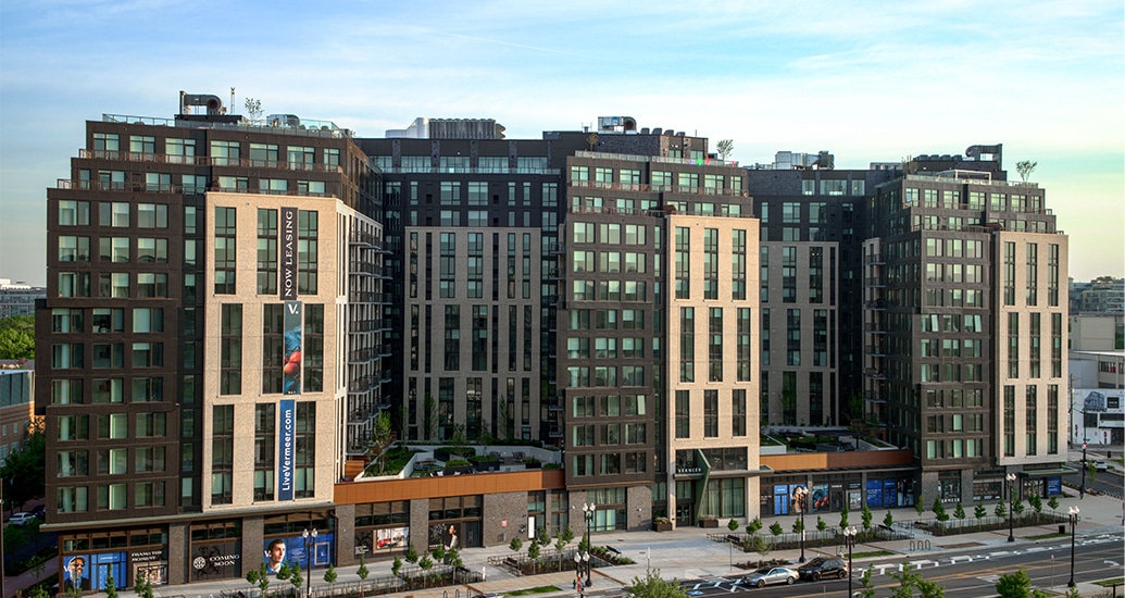 The exterior of a high-rise apartment building with a dark brown and beige facade and two elevated courtyards.