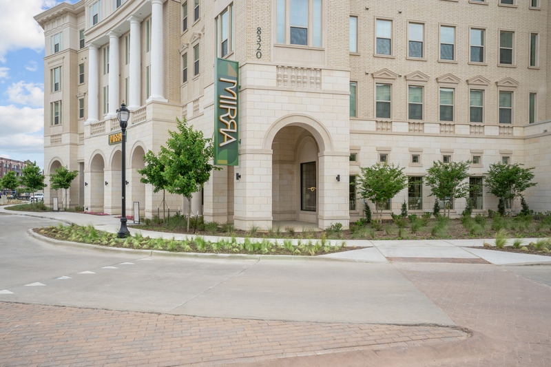 Exterior of an apartment building with tan and white brick, white columns, and a vertical sign that says "Mirra".