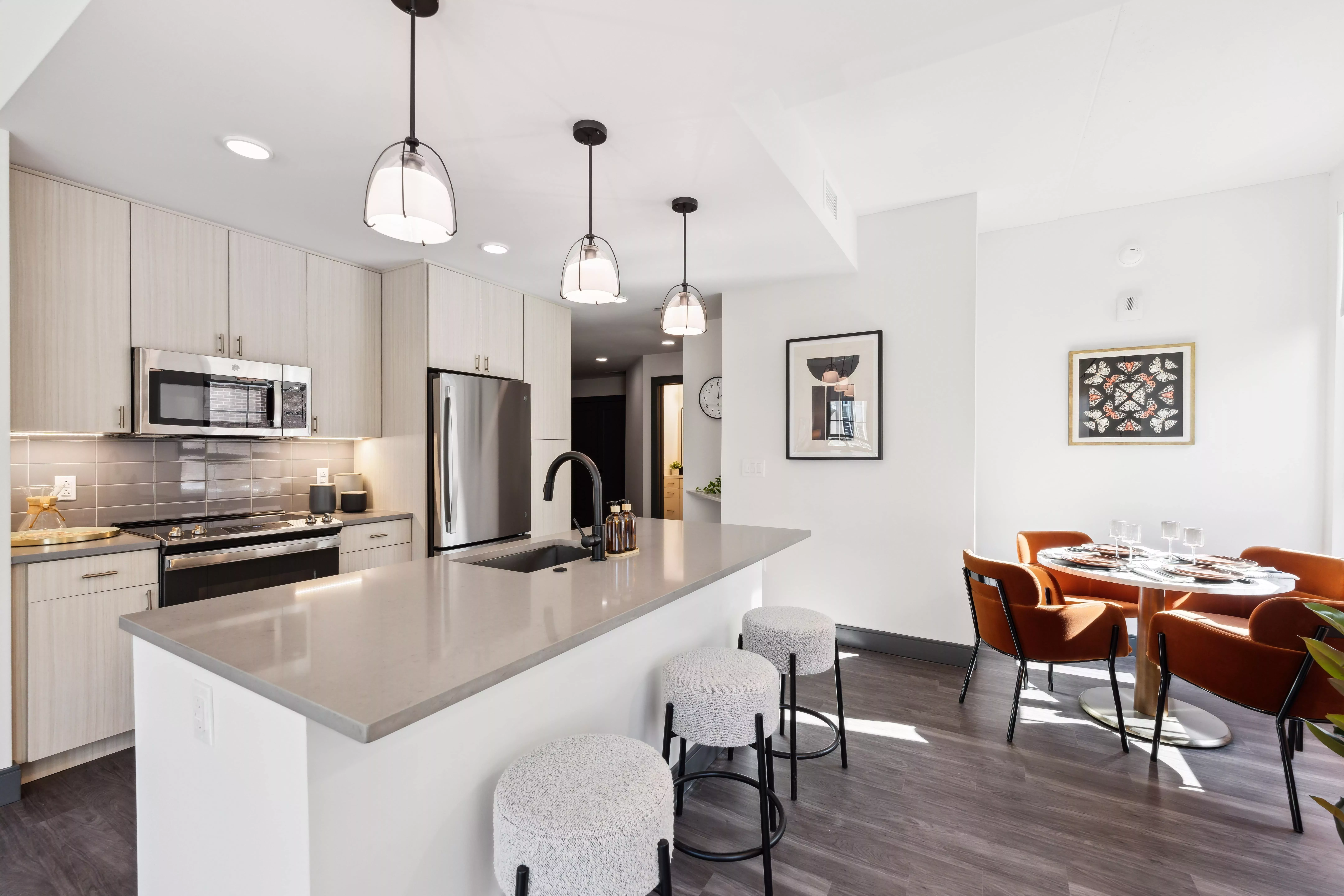 Kitchen with light color cabinets, dark wood-style floors, white walls, and hanging lights and a dining table with dark orange chairs