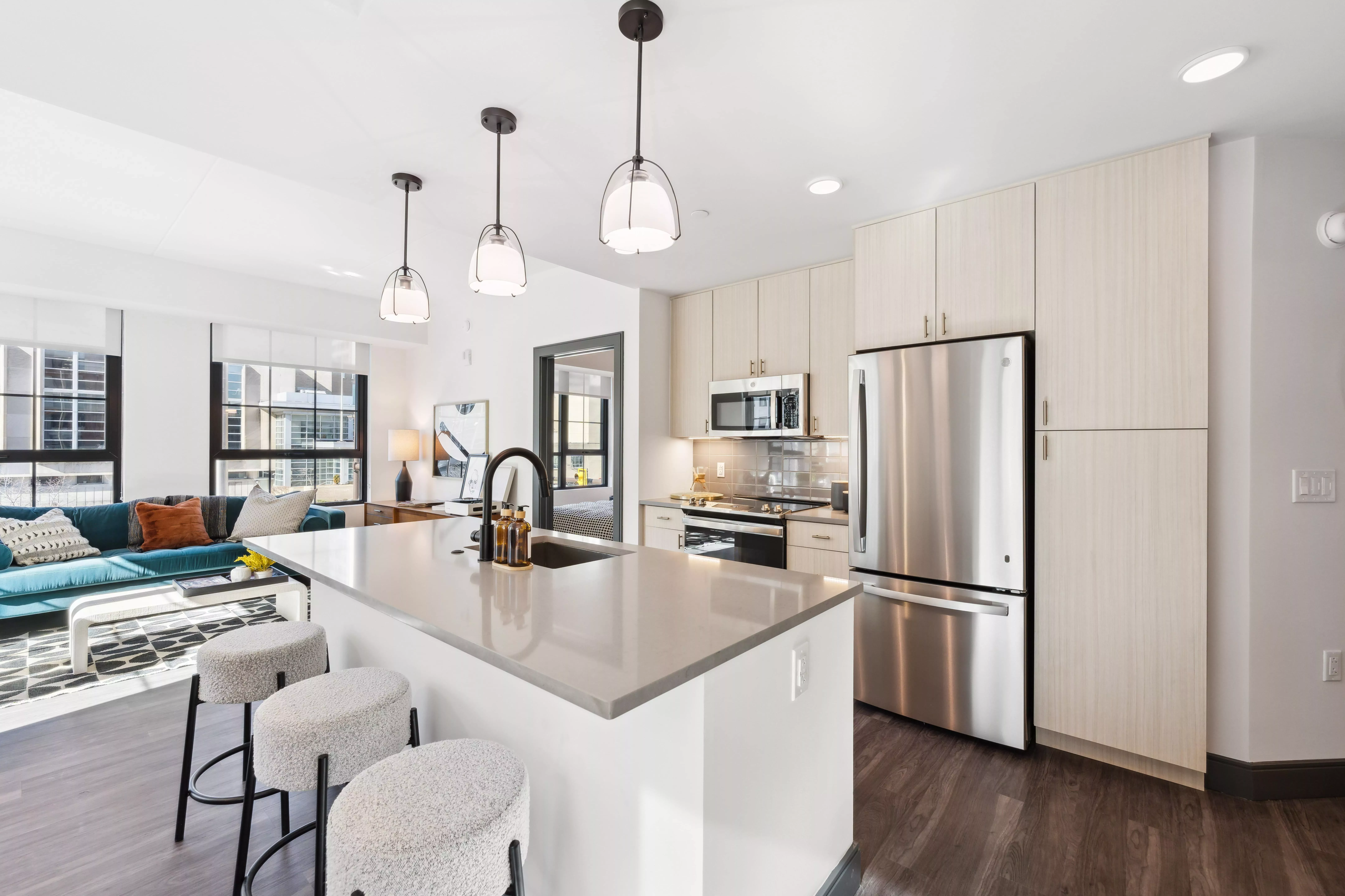 Kitchen with light color cabinets, dark wood-style floors, white walls, and hanging lights and a center island with sink
