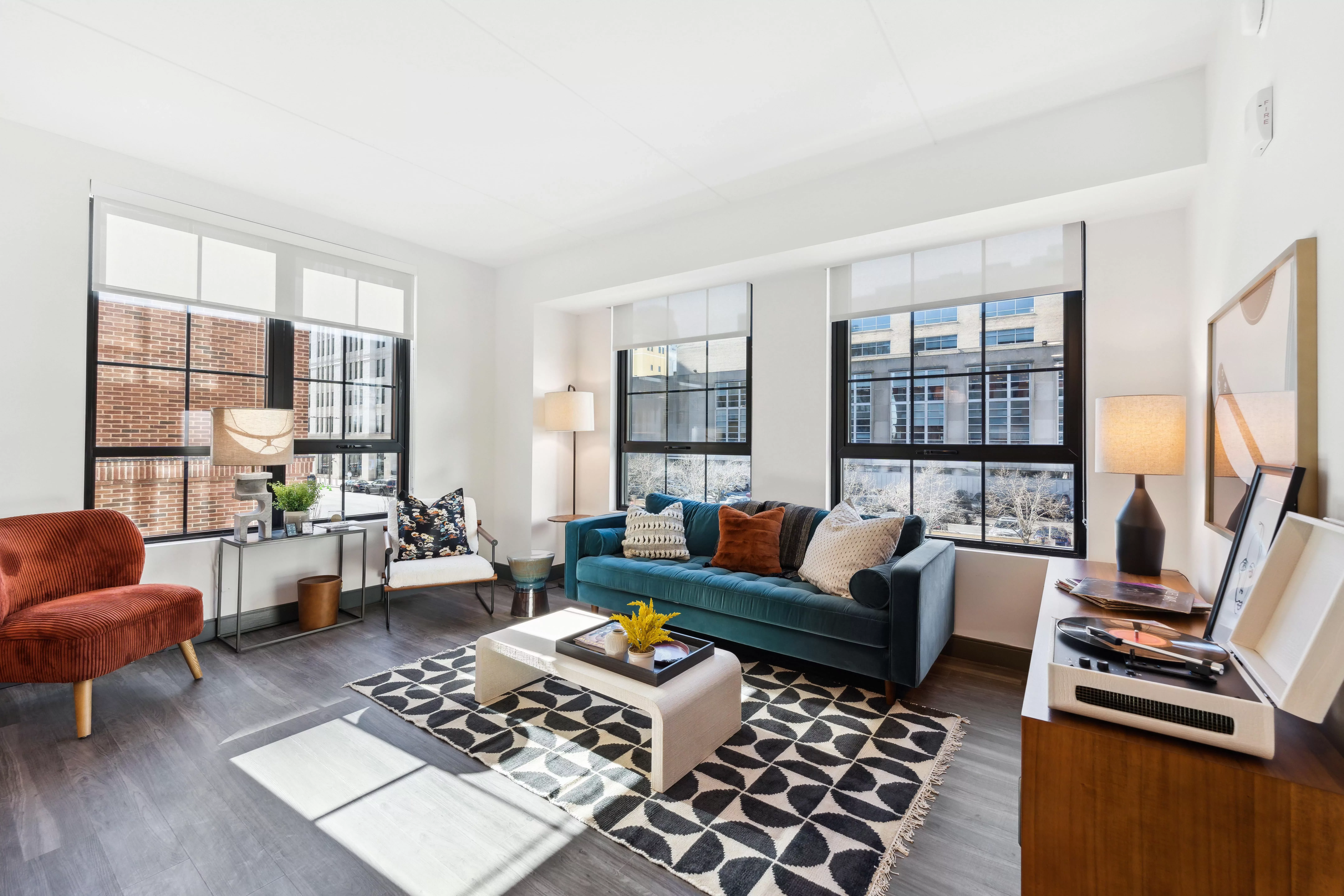 Living room with large, black-framed windows, dark hardwood-style floors, and velvet couch and chair