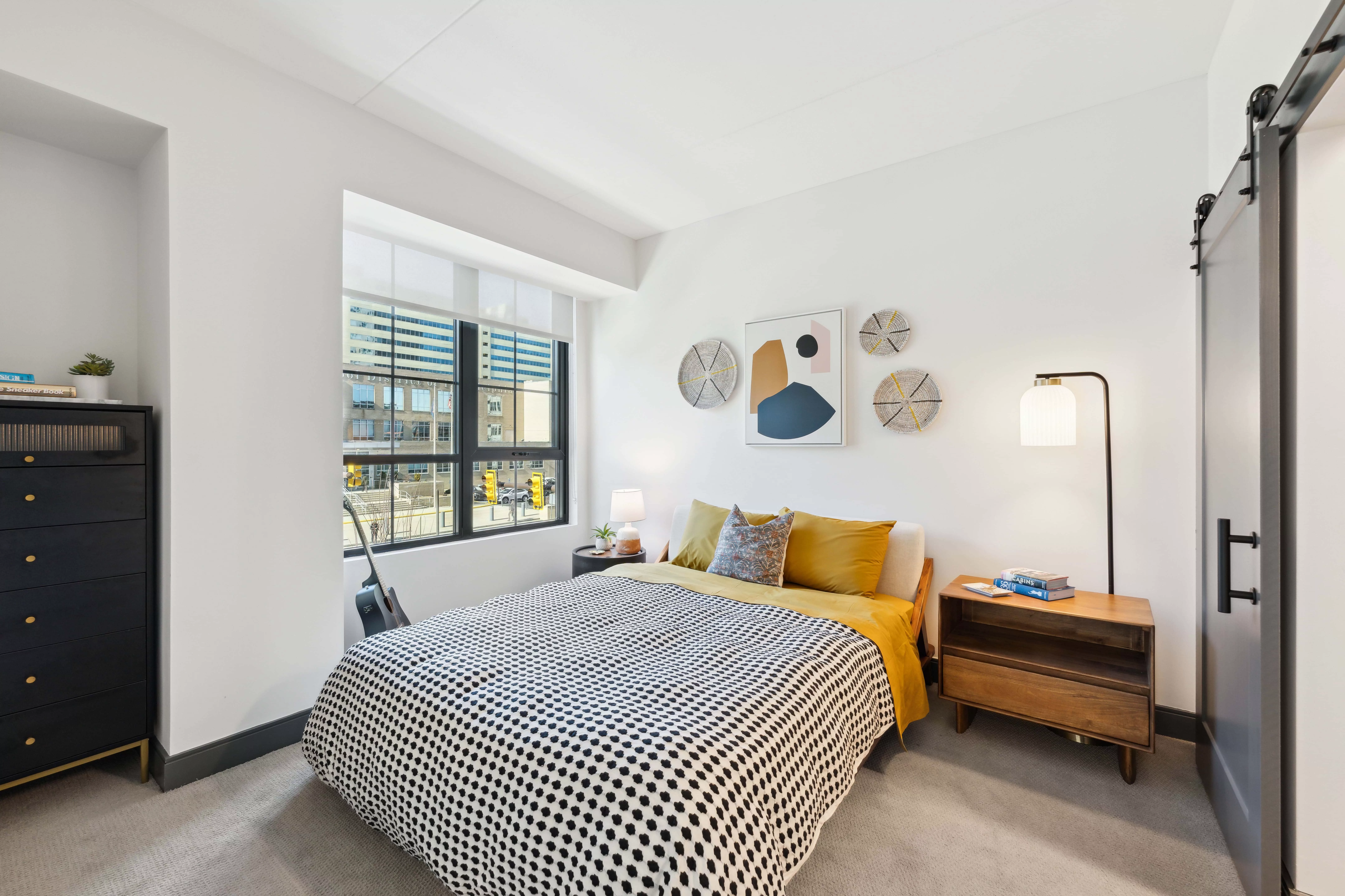 Bedroom with white walls, black-framed windows, and light colored carpet with a bed, dresser, and night stands