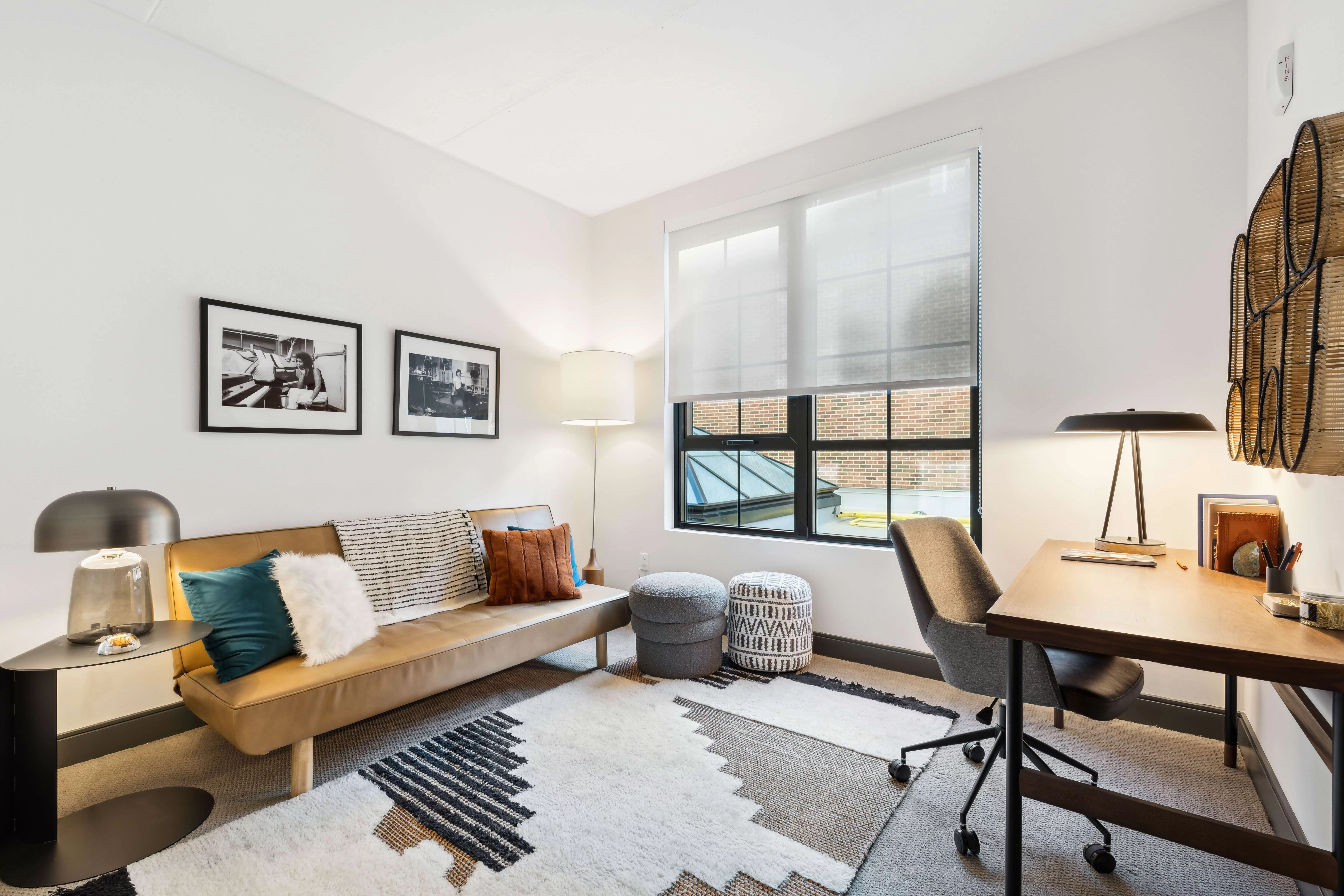 Bedroom with white walls and light-colored carpet with a tan couch and desk with rolling chair