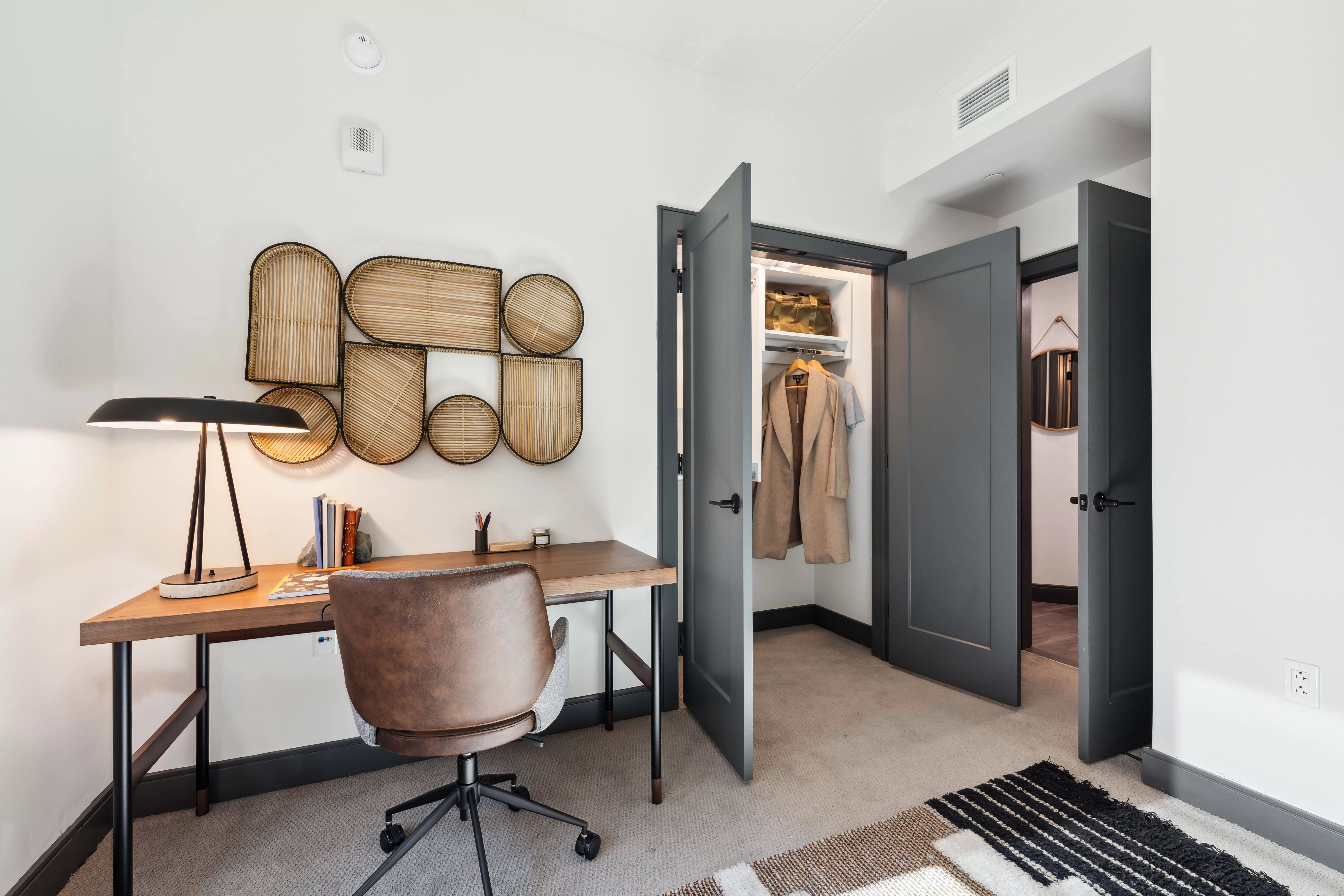 Bedroom with white walls and light-colored carpet with a desk and rolling chair, decoration wall art, and a closet with the doors open