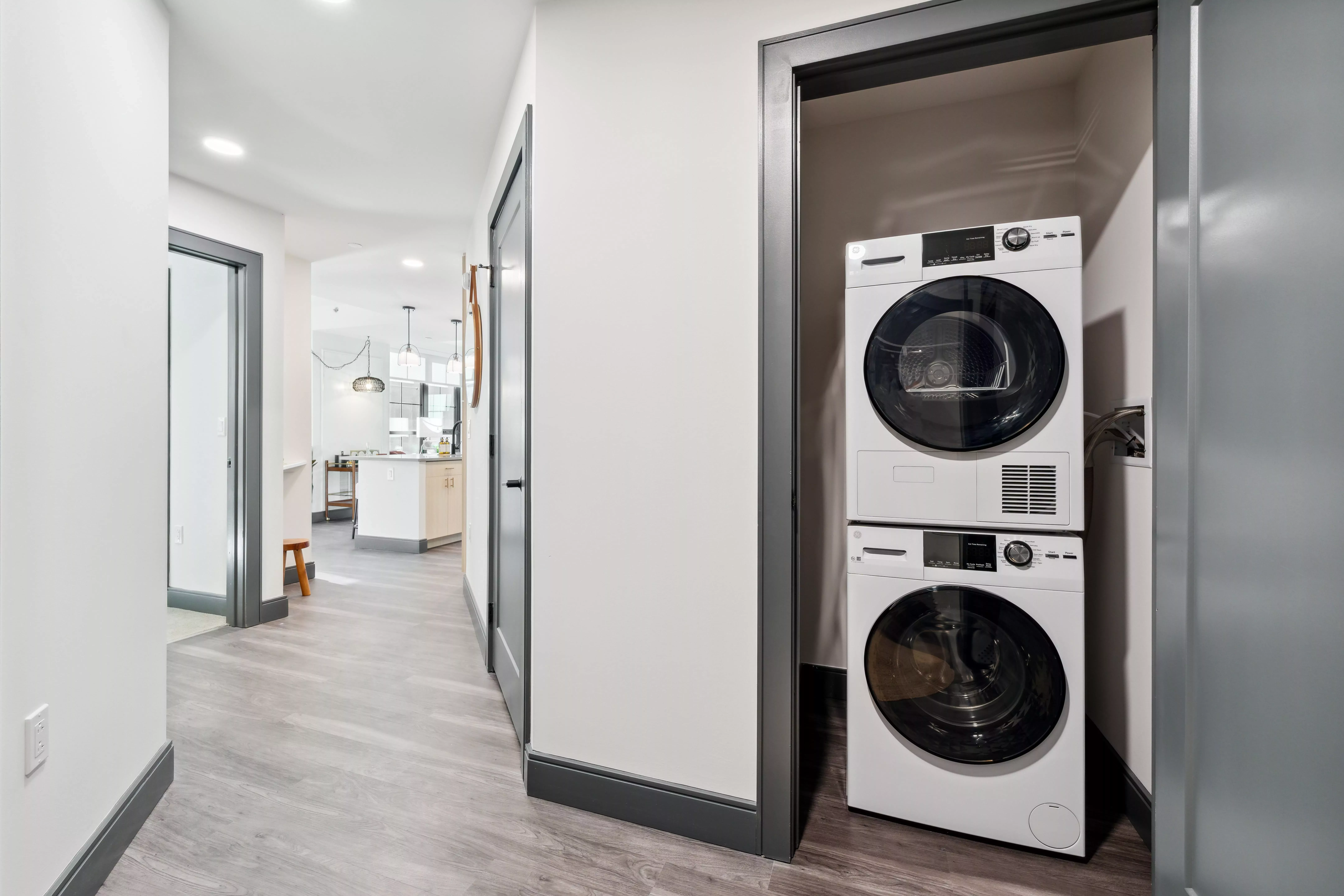 Hallway with white walls, dark wood-style floors, and a door open to show a stacked washer and dryer