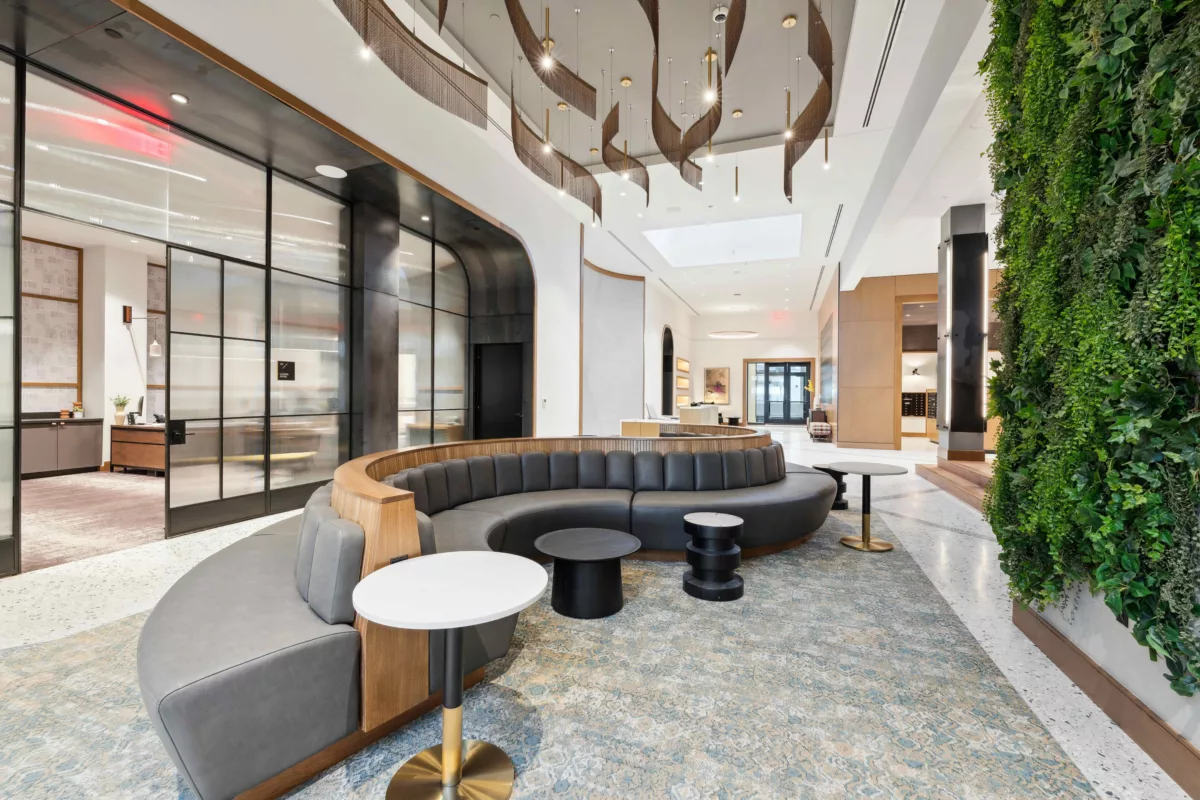 Lobby with curved gray couch, small tables, and greenery hanging from the wall