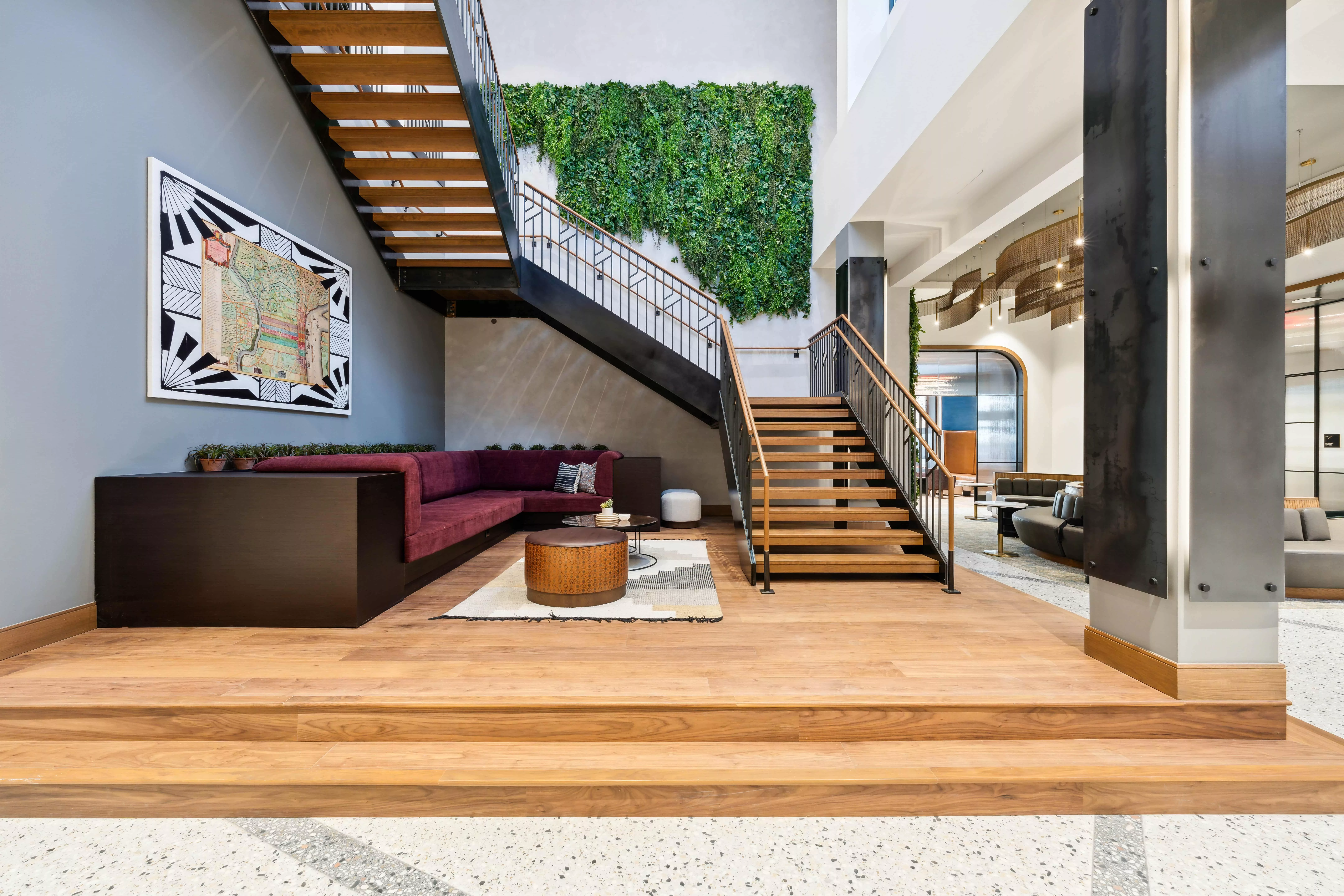 Lobby with wooden staircase, wall with hanging greenery, and artwork on the wall