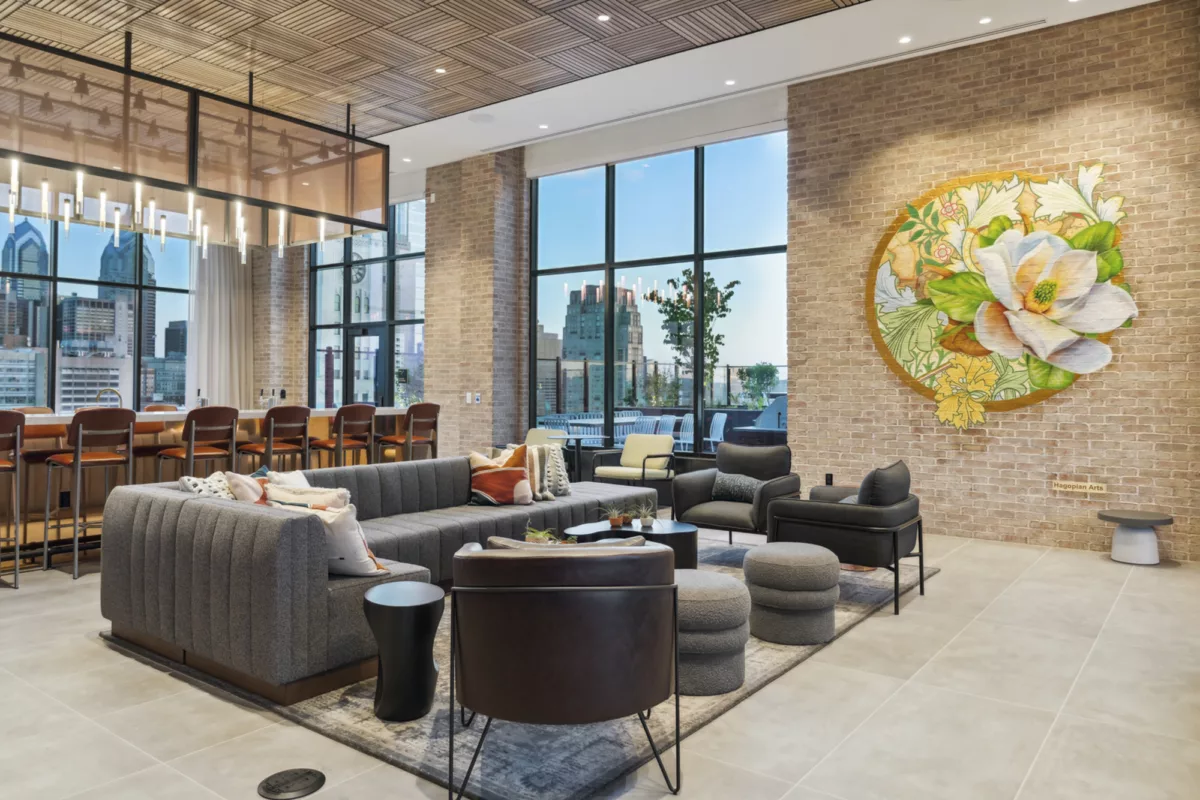 Rooftop lounge with bar, comfortable seating, mural on a brick wall, and views of the city skyline.