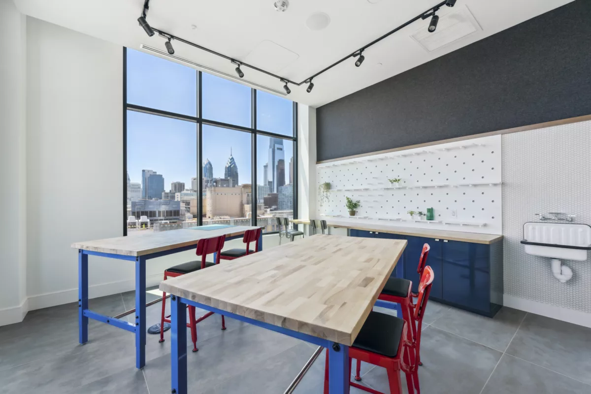 Maker's space with high top wooden tables, blue cabinets, and large windows with city views