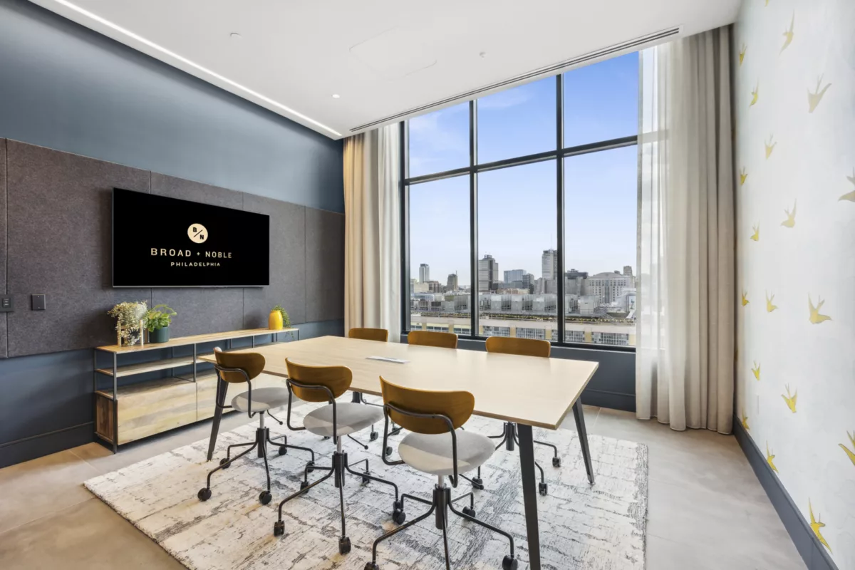 Private conference room with TV screen, table, rolling chairs, and large windows with city views