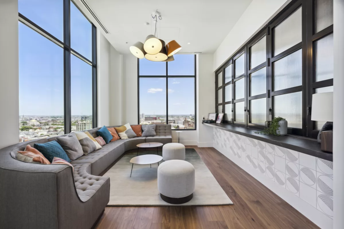 Rooftop lounge with large gray couch with multi-colored pillows and large windows with city views