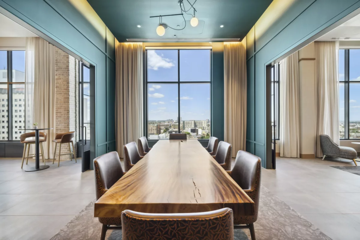 Rooftop private dining room with dark teal walls, long wooden table, chairs, and large windows with city views