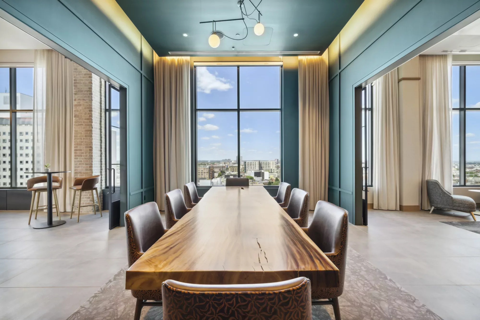 Rooftop private dining room with dark teal walls, long wooden table, chairs, and large windows with city views