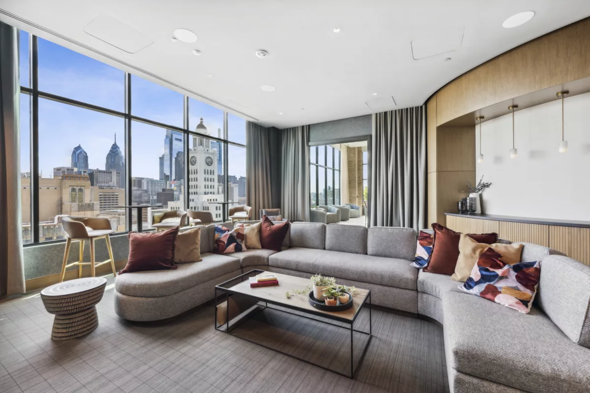 Rooftop lounge with gray couch, colorful pillows, and large windows with city views